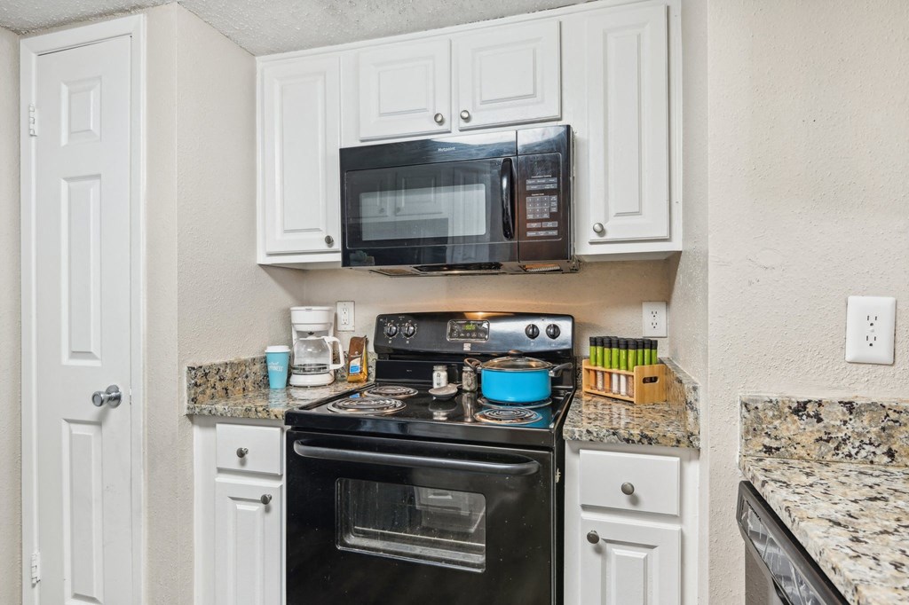 a kitchen with white cabinets and a black stove and microwave at The Glen at Highpoint, Dallas, 75243