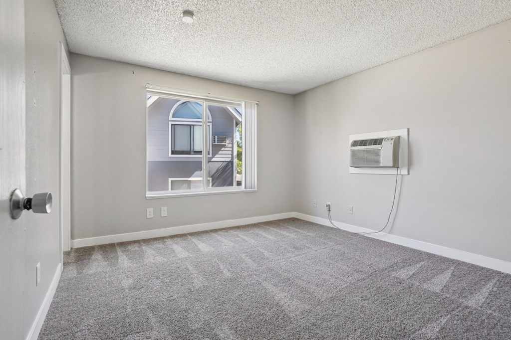 A room with a carpeted floor and a window overlooking a house.
