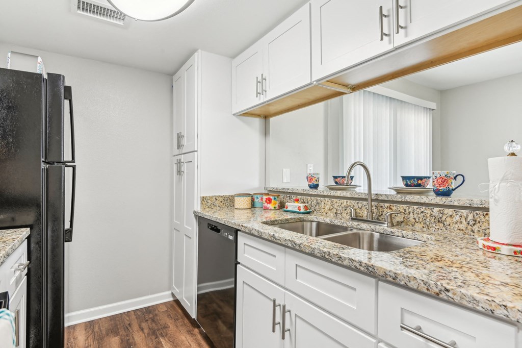a kitchen with white cabinets and granite counter tops and a black refrigerator at The Glen at Highpoint, Dallas, 75243
