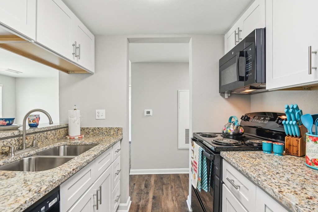 a kitchen with white cabinets and granite counter tops and a black microwave at The Glen at Highpoint, Dallas, 75243