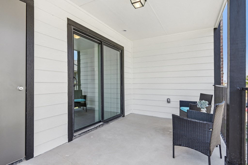 a covered patio with two chairs and a sliding glass door at The Glen at Highpoint, Dallas, 75243