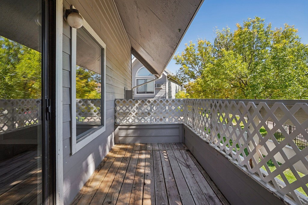 A wooden deck with a lattice fence and a view of a house and trees.