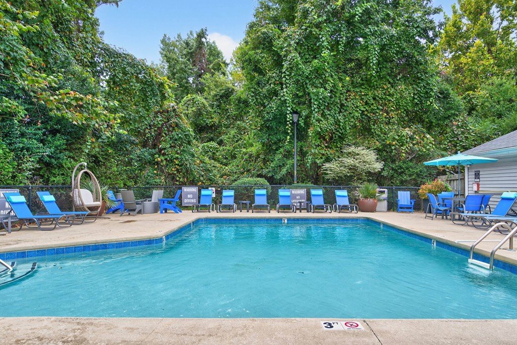 A pool surrounded by trees and chairs.at Lofts of Wilmington Apartments, Wilmington, North Carolina