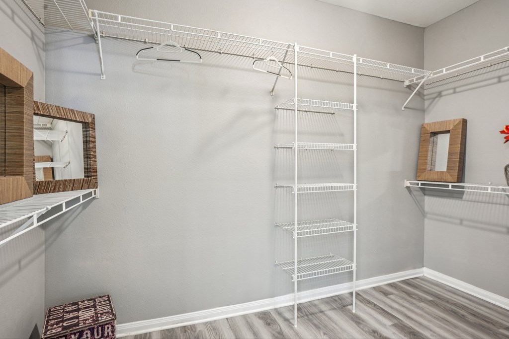 A walk-in closet with white shelving and a mirror on the wall.