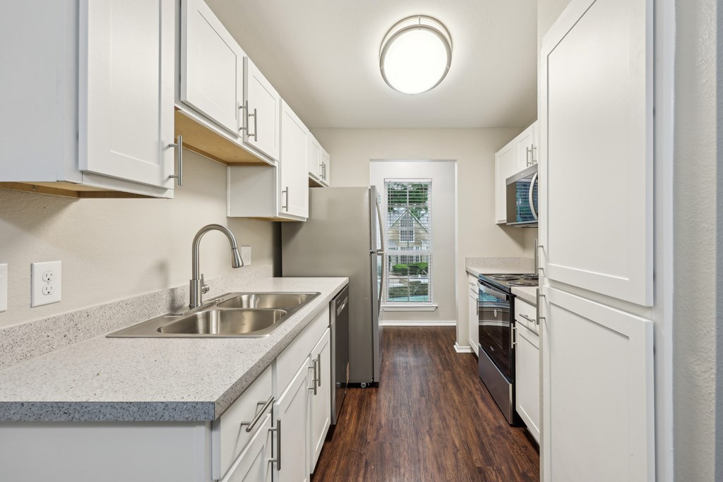 A kitchen with white cabinets and a wooden floor at The Willows on Rosemeade, Dallas, TX 75287
