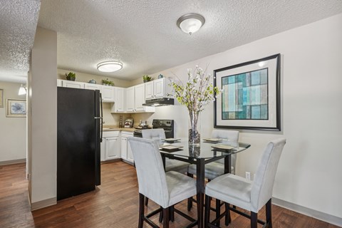 A black fridge is in a white kitchen with a glass table and chairs.
