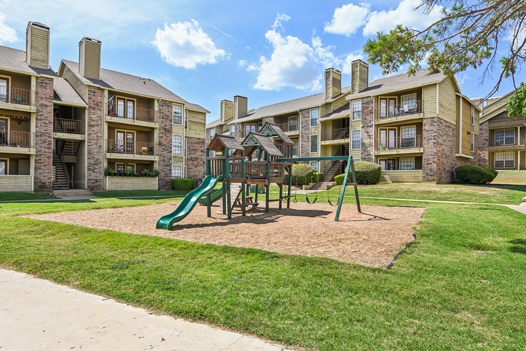 A playground with a green slide and a brown sandbox in front of apartment buildings. at The Glen, Texas, 75067