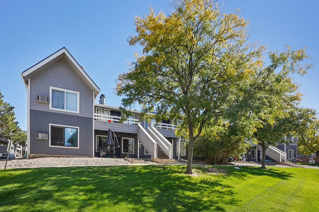 A grey house with a tree in front of it.