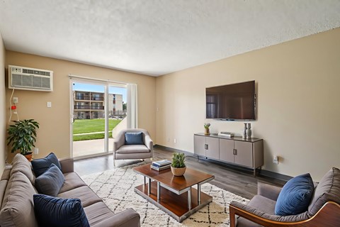 A living room with a brown couch, a grey armchair, a wooden coffee table, and a flat-screen TV mounted on the wall.
