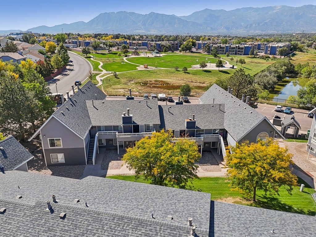 A large house with a grey roof is surrounded by other houses and trees.