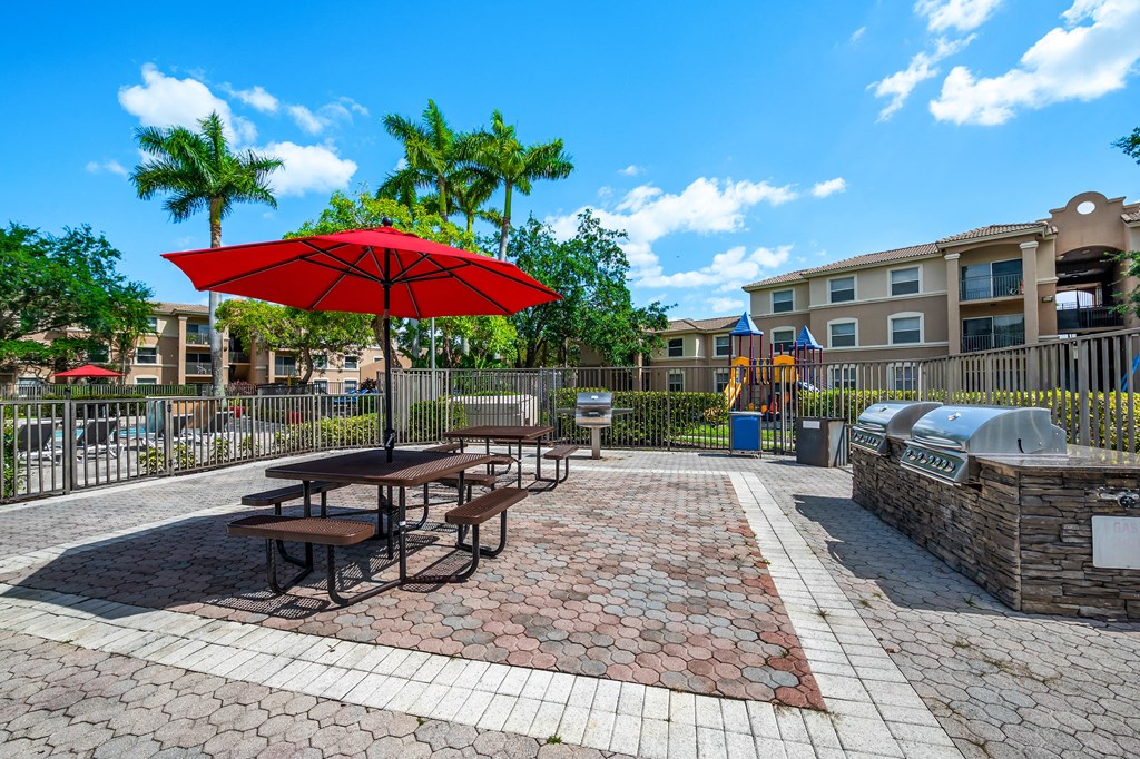 a picnic area with picnic tables and an umbrella in front of an apartment building at Pembroke Pines Landings, Pembroke Pines, FL, 33025