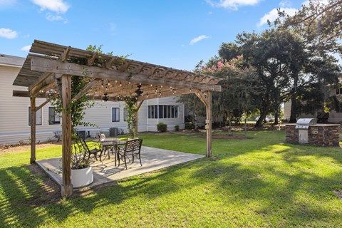 A wooden pergola with a table and chairs under it. at River Crossing Apartments, Thunderbolt, GA