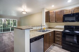 A kitchen with brown cabinets, black stove and stainless dishwasher at Arcadia Townhomes, Federal Way, WA - Photo Gallery 4