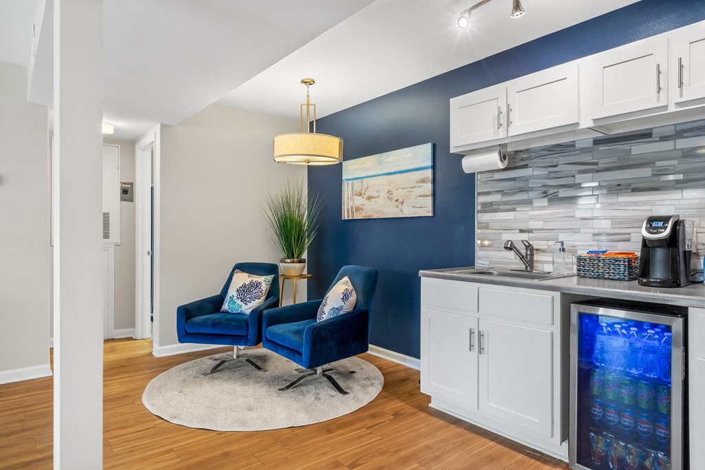 Clubhouse area with two blue chairs and a kitchen with a sink at Lofts of Wilmington Apartments, Wilmington, NC