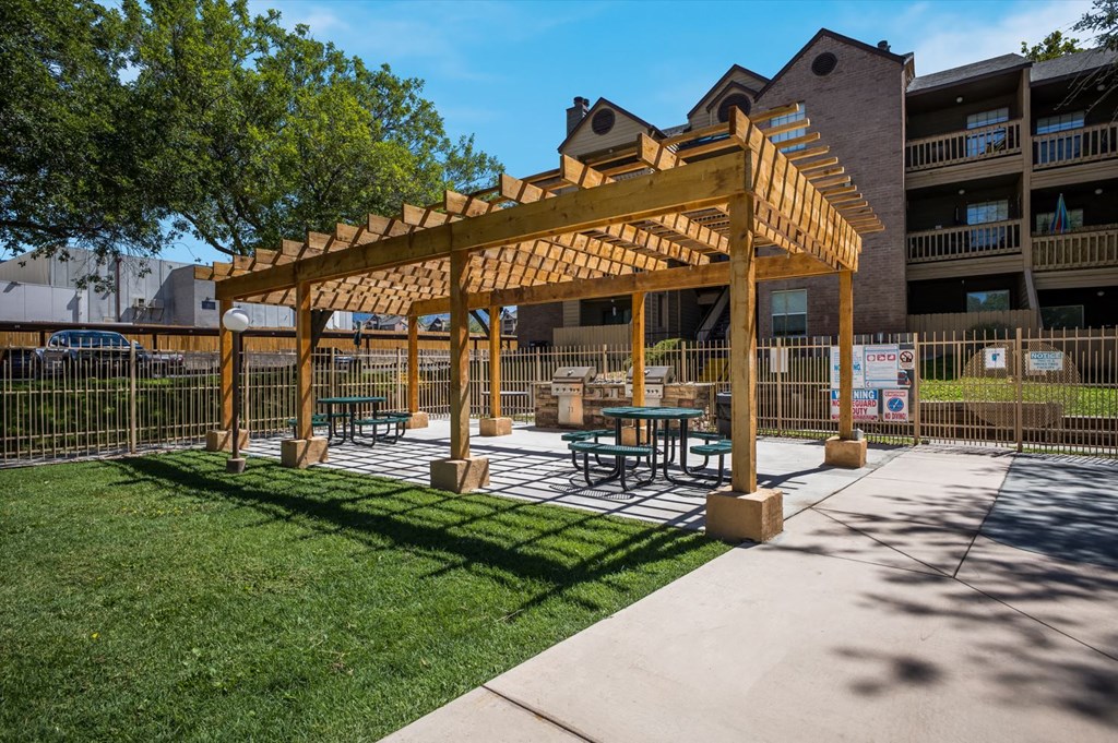 Outdoor wooden pergola with a table and chairs under and BBQ grills at Mountain Run Apartments, Albuquerque