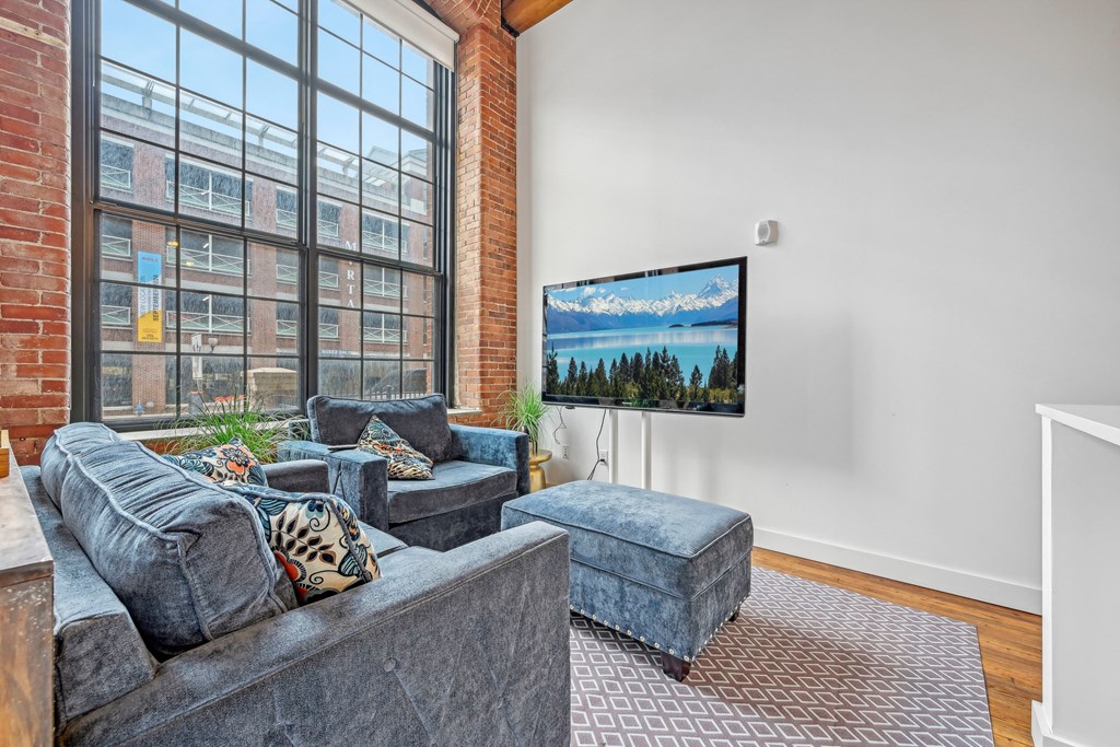 a living room with a large window and a couch and a chair at Riverwalk Apartments, Lawrence, MA