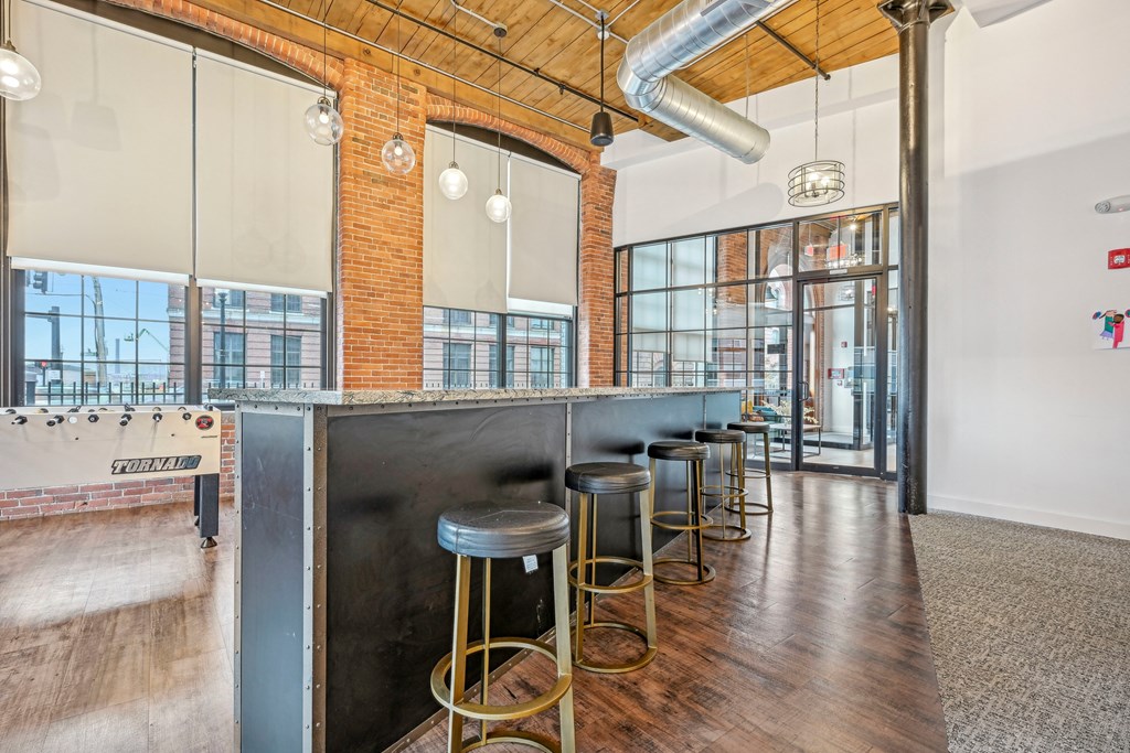 a long bar with stools and a exposed brick wall and glass doors at Riverwalk Apartments, Lawrence, MA