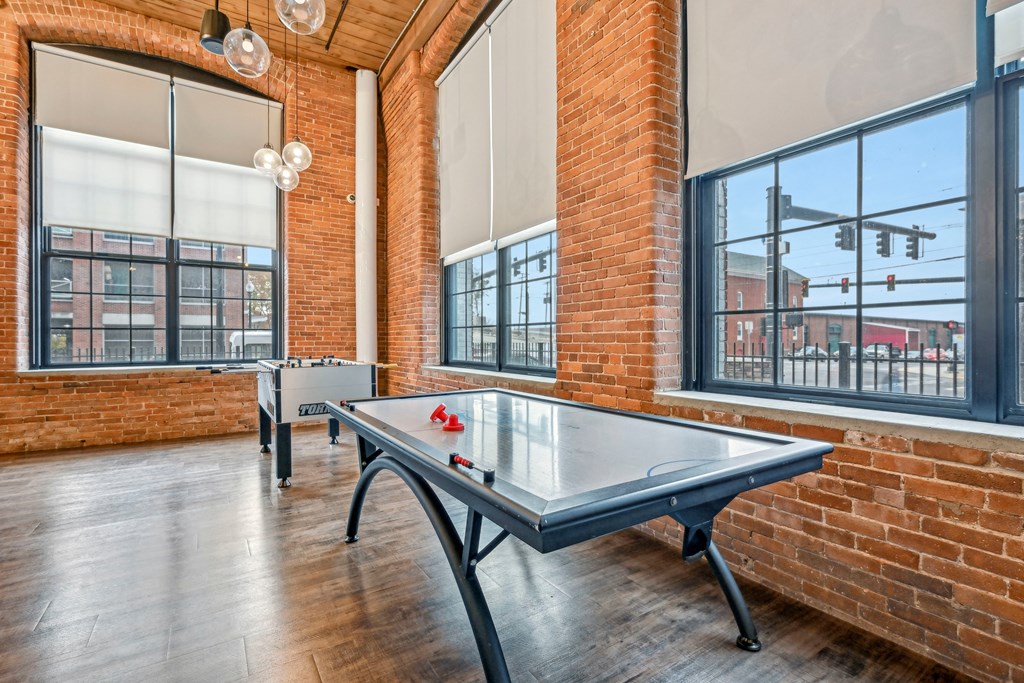 two ping pong tables in an empty game room with brick walls and large windows at Riverwalk Apartments, Lawrence, MA