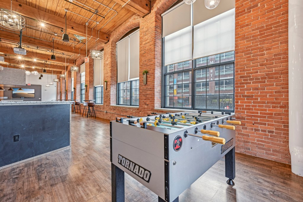 a foosball table in a room with brick walls and a bar at Riverwalk Apartments, Lawrence, MA