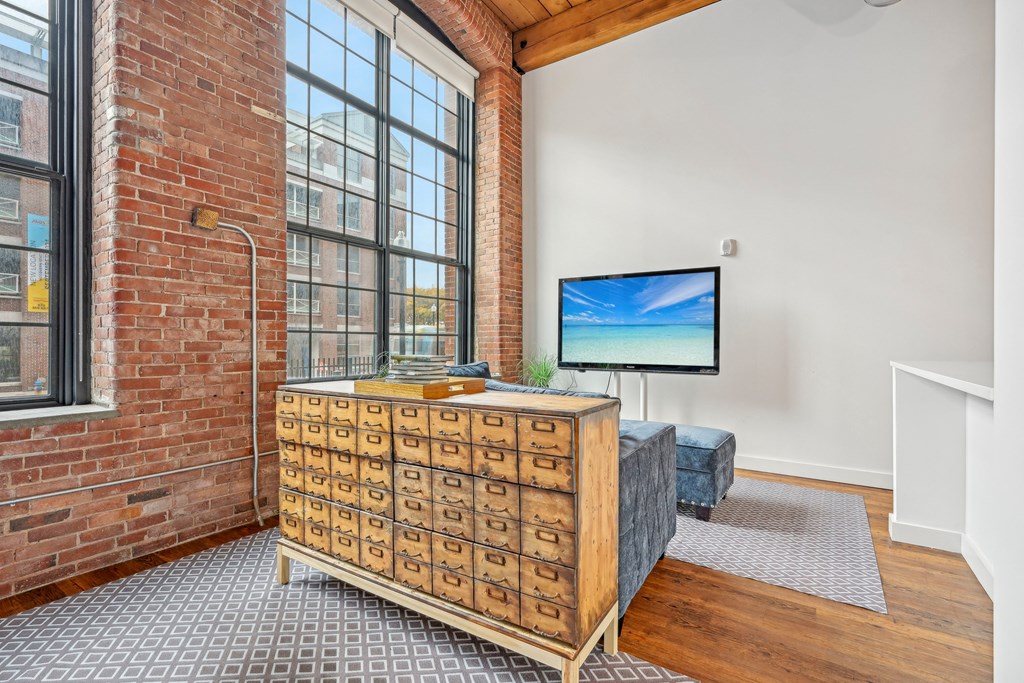 a living room with a large window and a dresser with a tv on it at Riverwalk Apartments, Lawrence, MA