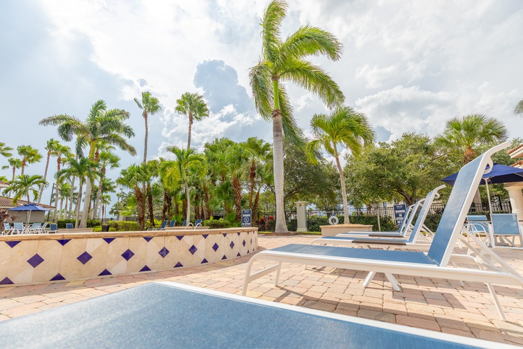 a resort style pool with chaise lounge chairs and palm trees in the background at Heritage Bay, Jensen Beach, 34957