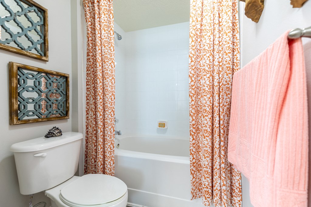 a bathroom with a white toilet next to a bathtub with a orange shower curtain at Heritage Bay, Florida, 34957