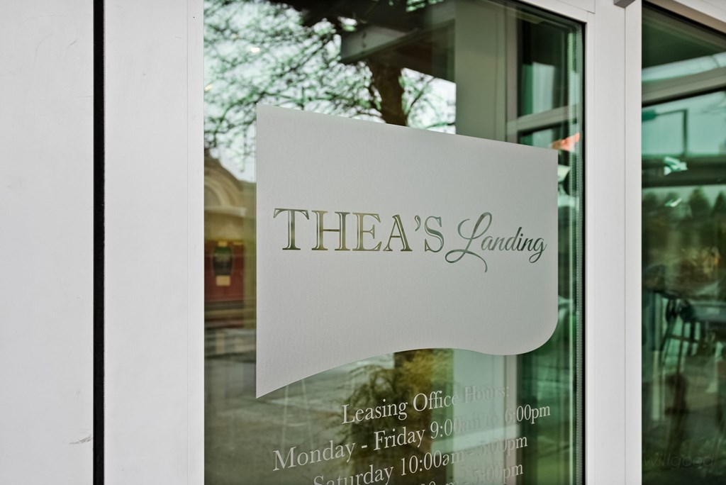 A window with a sign that says "Thea's Laundry" and the business hours listed below it.