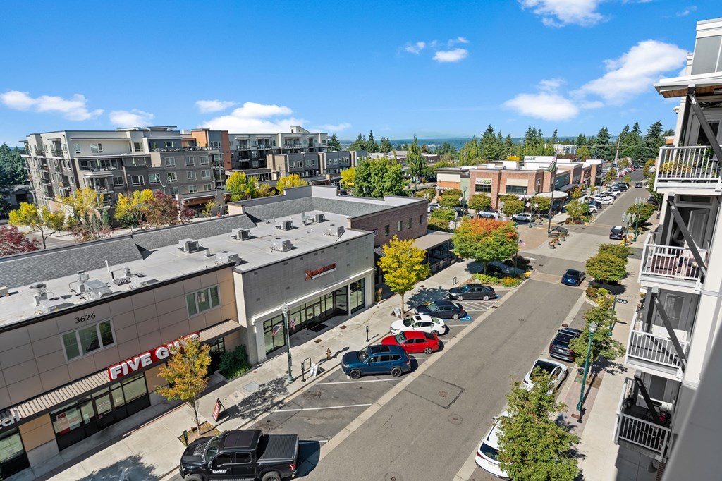 A street view of a shopping area with cars parked on the side of the road.