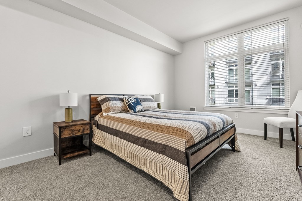 A bedroom with a bed, nightstand, and window.