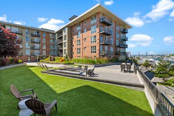 A large grassy area with chairs and a table in front of apartment buildings.
