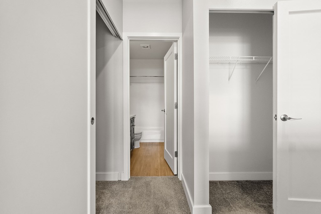 A white hallway with a door on the right and a toilet in the distance.