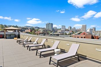 A row of sun loungers are on a roof terrace overlooking a city skyline.