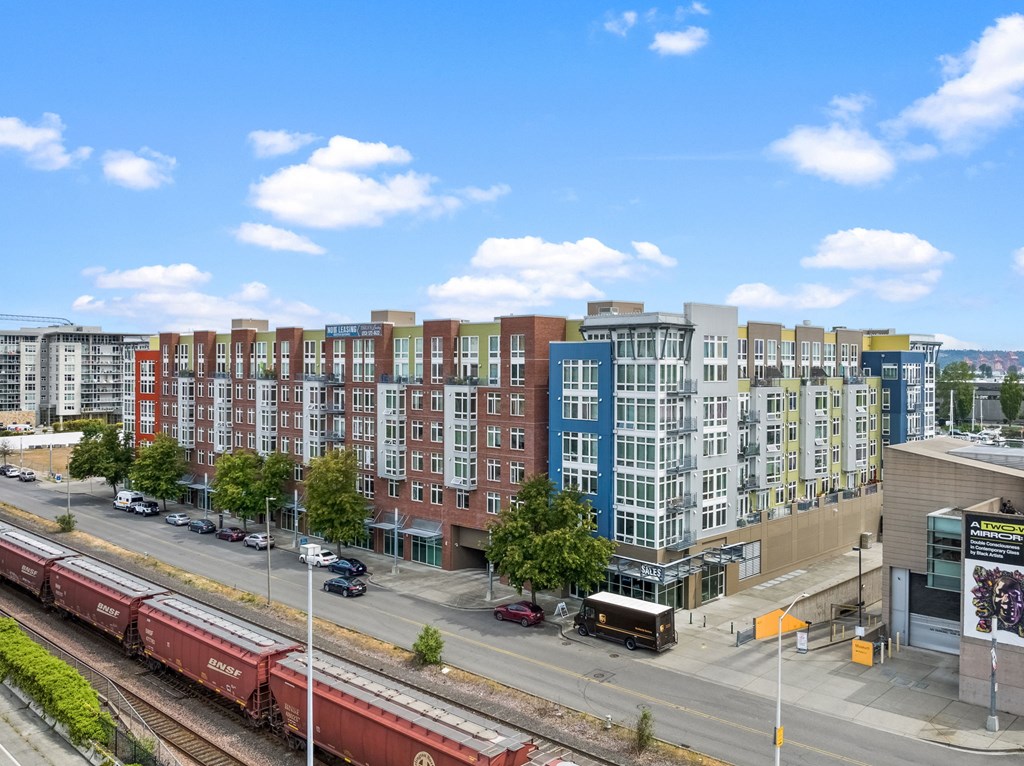 A train is on the tracks in front of a row of colorful buildings.