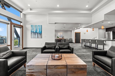 A modern living room with a large wooden coffee table and black leather chairs.