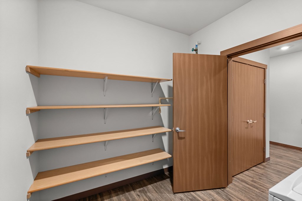 A room with a white wall and a brown shelving unit.