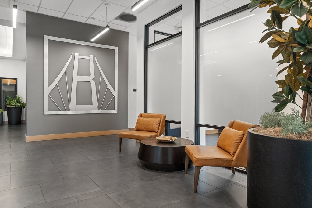 A modern office lobby with a large abstract artwork on the wall, two brown leather chairs, and a round coffee table.