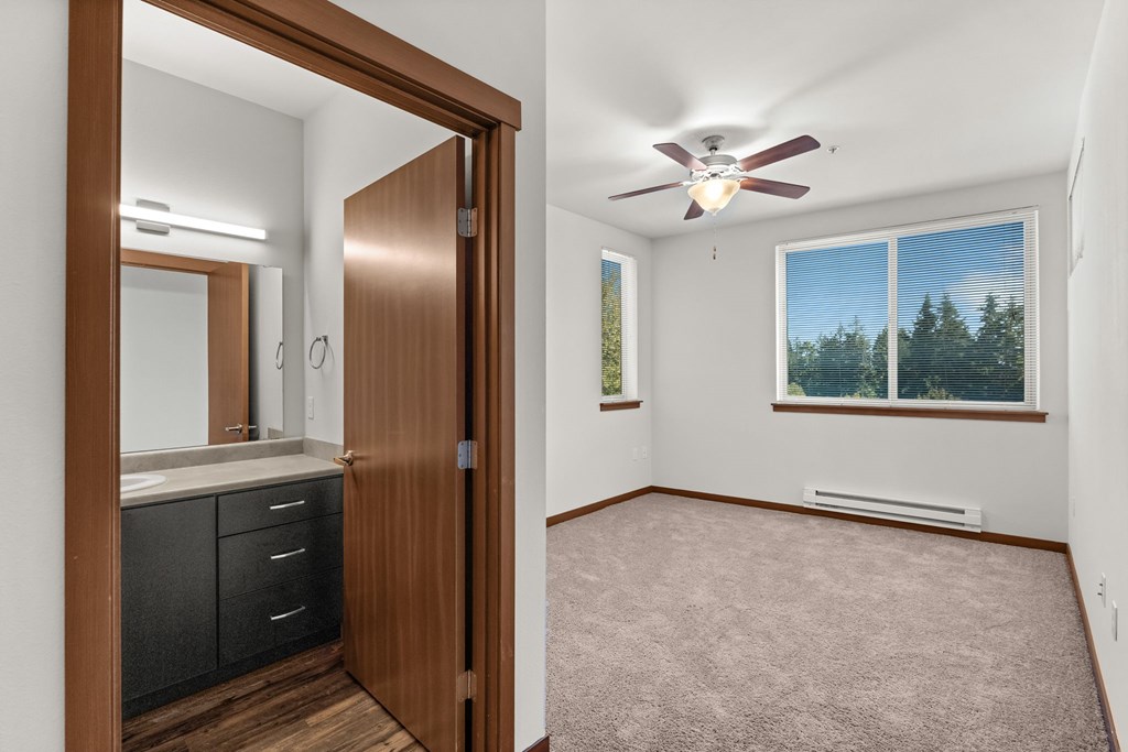 A room with a ceiling fan and a window showing trees outside.
