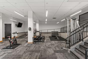 A gym with a variety of equipment including treadmills, weights, and a staircase.