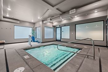 A person is standing by the pool in a room with large windows.