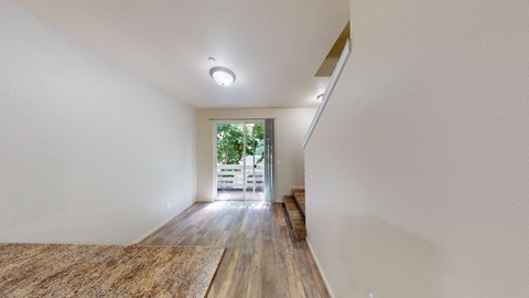 a long hallway with white walls and wood floors and a door to a patio