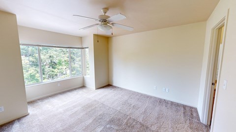 an empty living room with a large window and a ceiling fan