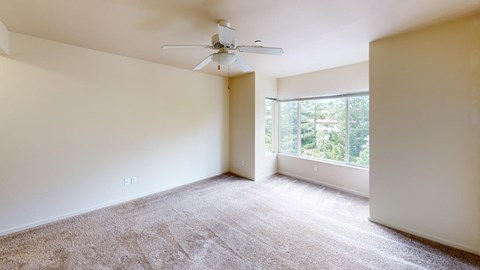 an empty living room with a large window and a ceiling fan