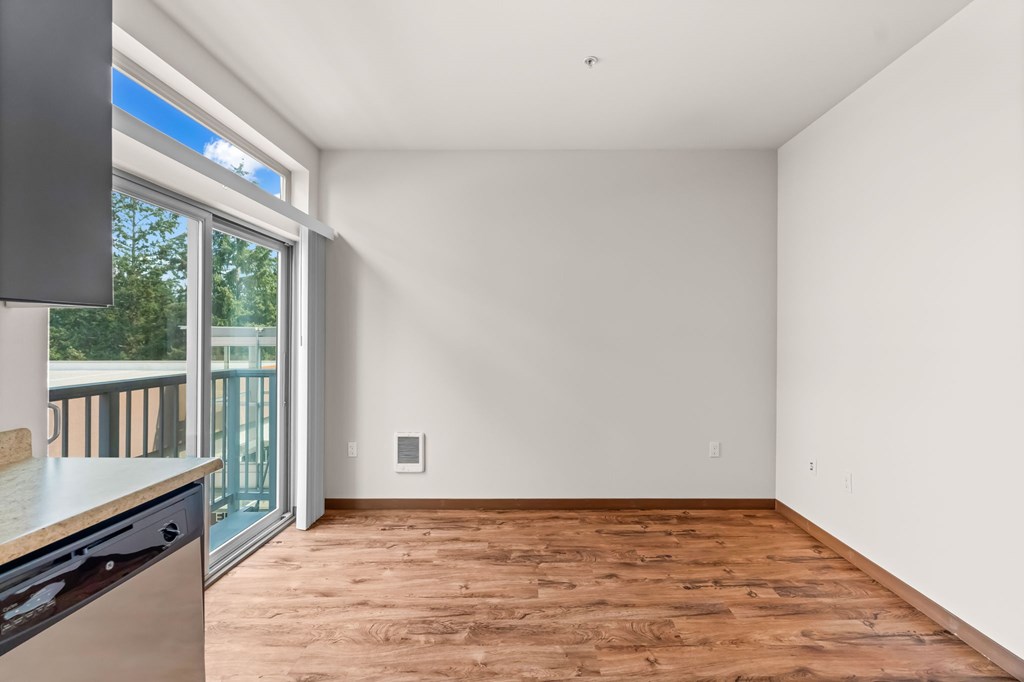 A kitchen with a wooden floor and a window overlooking a balcony.