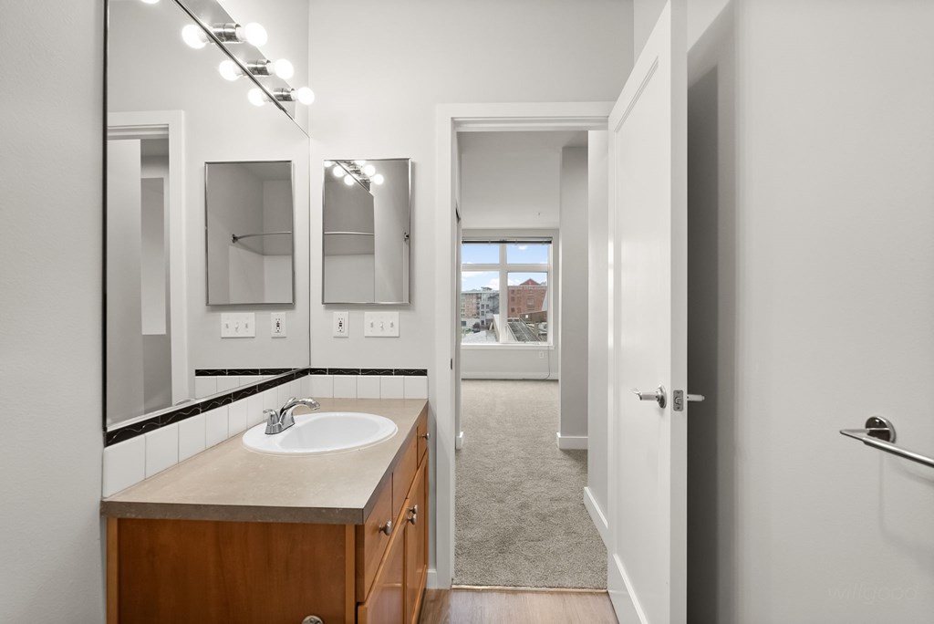 A bathroom with a sink, mirrors, and a door leading to a hallway.