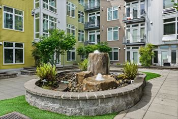 A fountain in the middle of a garden surrounded by a stone wall.