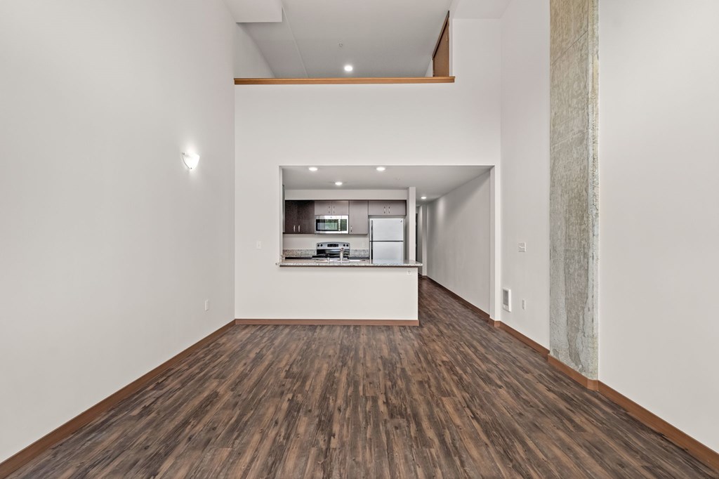 A room with wooden floors and a kitchen area in the background.