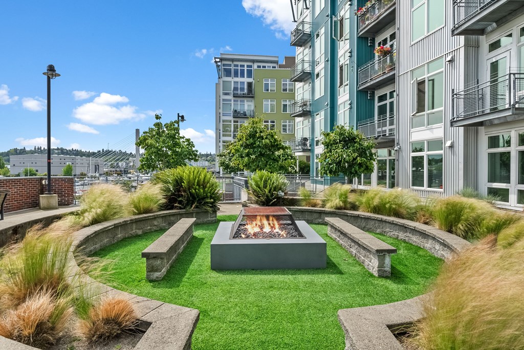 A modern outdoor fire pit is surrounded by a grassy area and concrete benches.