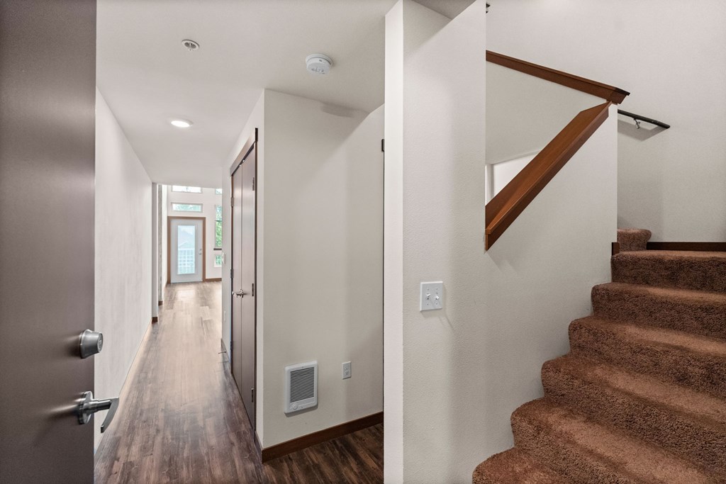 A hallway with a staircase on the right and a door on the left.