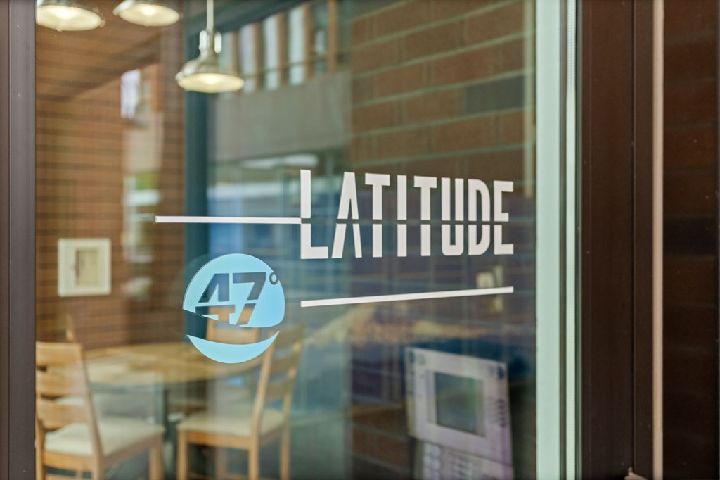 A window with a reflection of a room and the word "Latitude" on it.