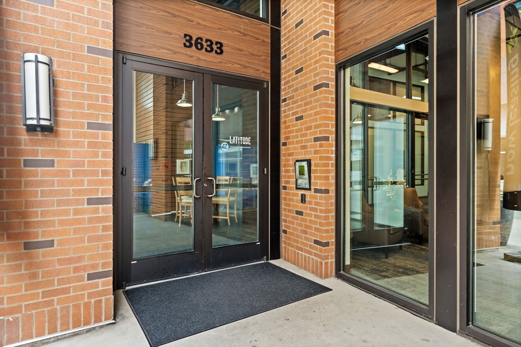 The entrance to a building with a glass door and a black mat on the floor.
